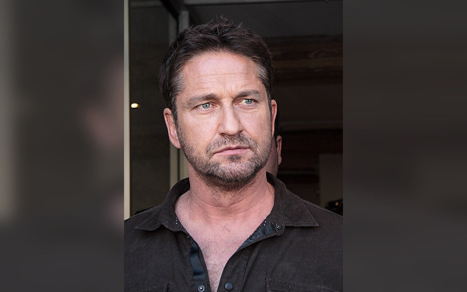 A man with short dark hair and stubble looks off to the side outdoors